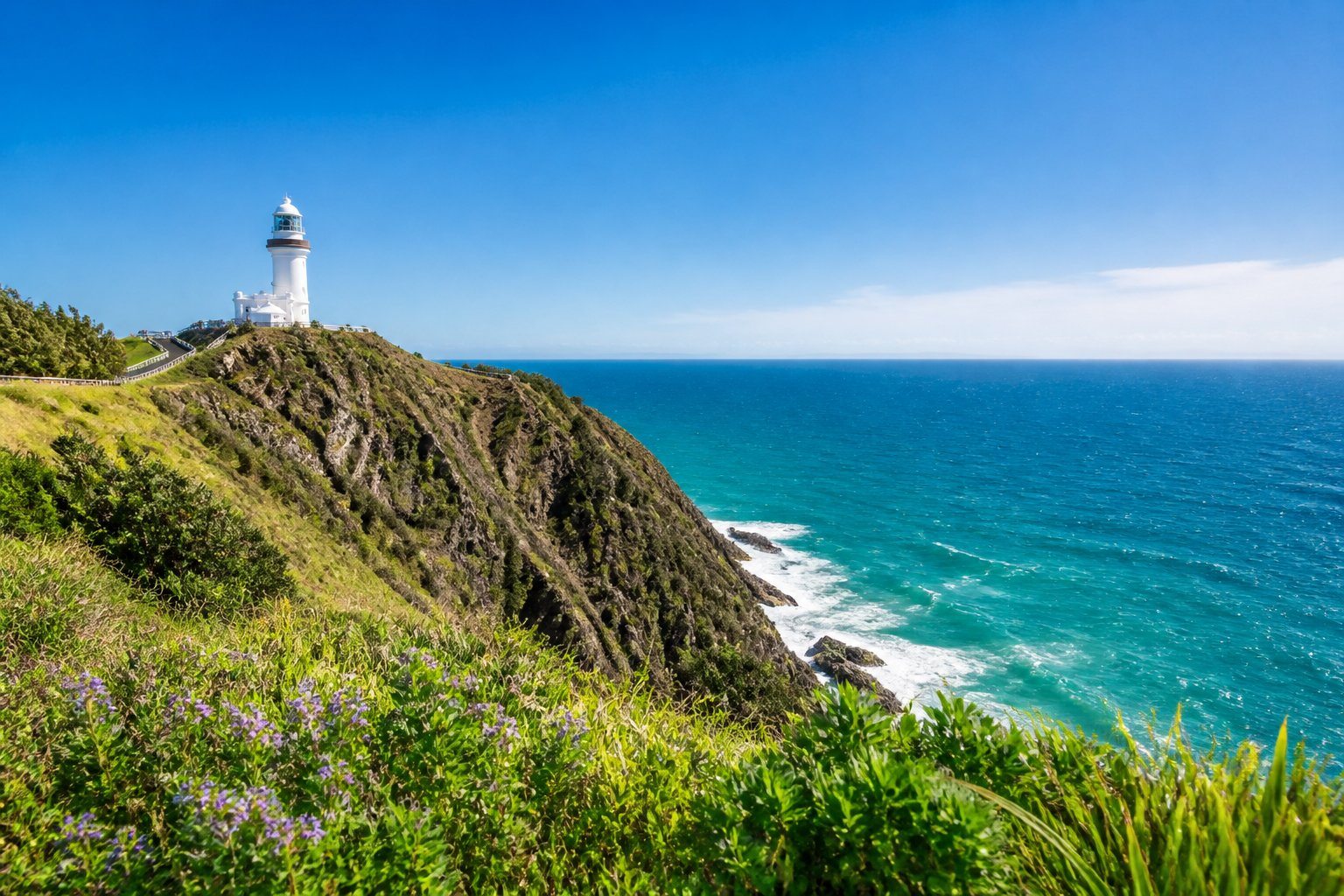Farol de Byron Bay sobre penhasco com oceano azul e vegetação costeira ao redor.