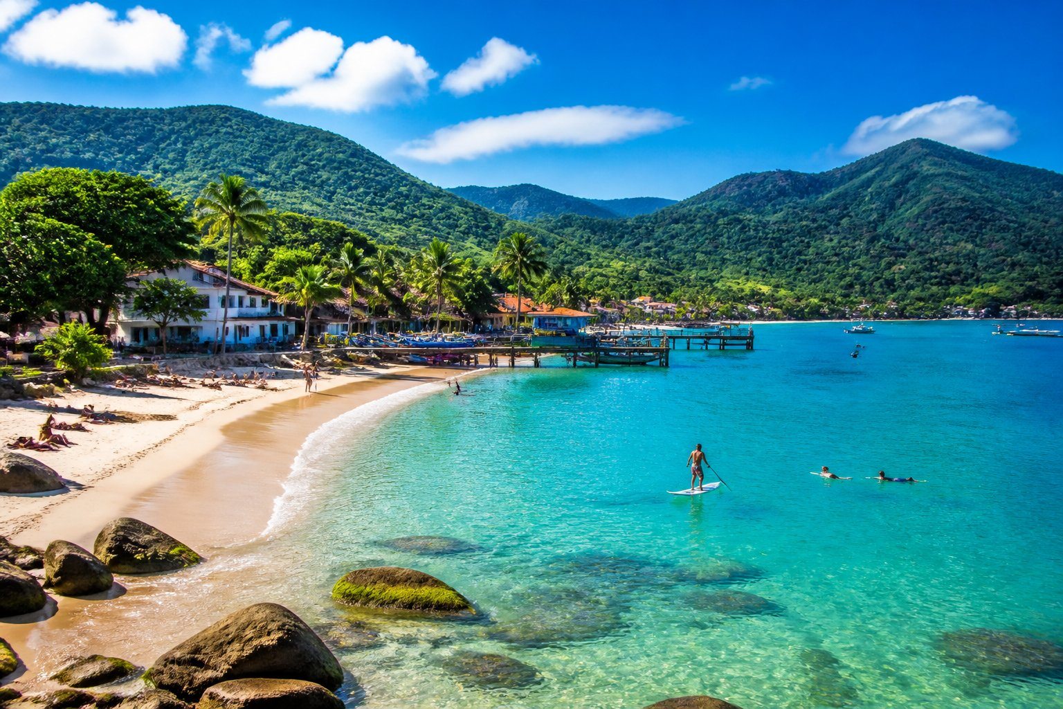 Praia de São Sebastião com mar azul, areia branca, vegetação verde e pessoas aproveitando atividades ao ar livre.