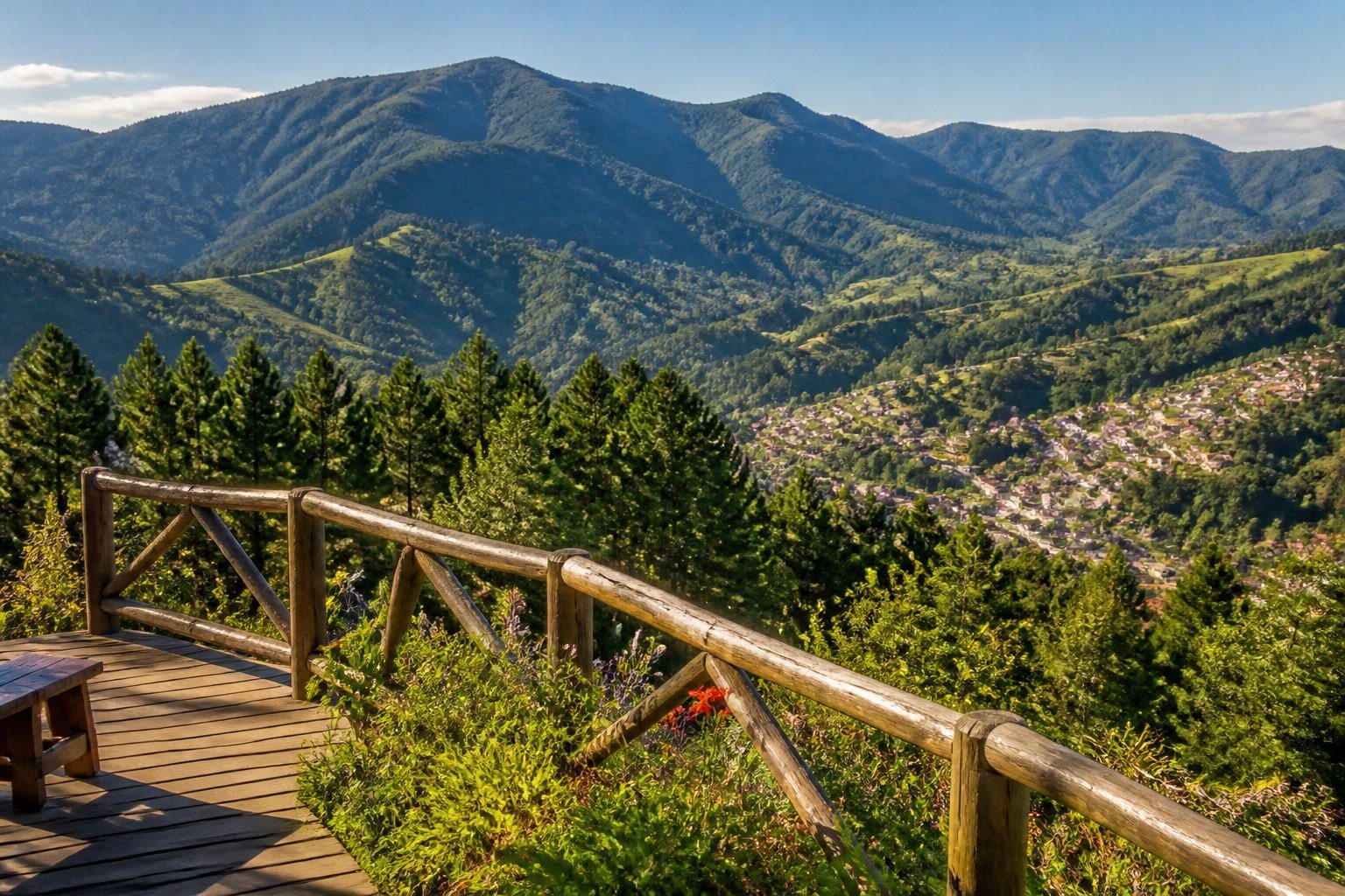 Vista panorâmica das montanhas verdes e floresta densa em Santo Antônio do Pinhal, com um deck de madeira em primeiro plano e uma pequena cidade ao fundo.